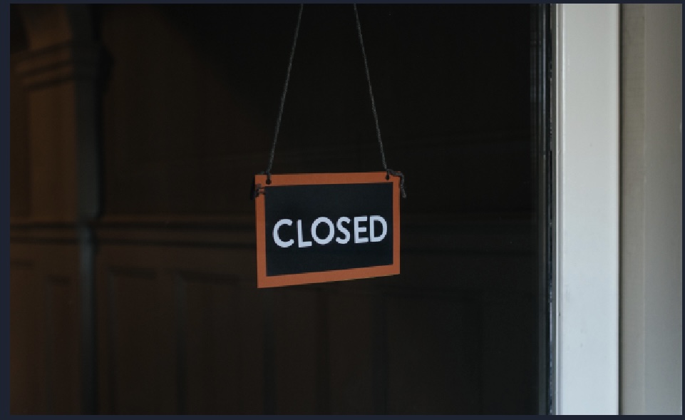 A dark photo of a “closed” sign hanging on a window with an orange border around it.