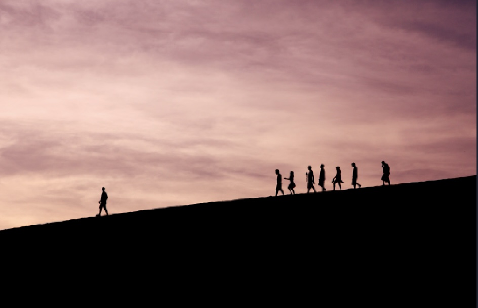 A silhouette of people on a hill against a pink sunset, with one person leading the others down.